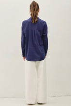 Load image into Gallery viewer, A woman viewed from behind wearing a navy blue long-sleeve button-up shirt and white wide-leg trousers, standing against a plain off-white studio background.
