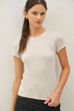 Load image into Gallery viewer, A woman wearing a fitted short-sleeve crewneck t-shirt in off-white, paired with dark jeans, photographed against a plain light gray studio background.