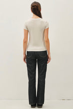 Load image into Gallery viewer, A woman viewed from behind wearing a fitted short-sleeve cream t-shirt and dark charcoal gray jeans, standing against a plain white studio background.