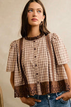 Load image into Gallery viewer, A woman wearing a brown and beige plaid short-sleeve blouse with dark brown lace trim at the collar and hem, paired with blue jeans, against a neutral beige background.
