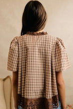 Load image into Gallery viewer, A woman viewed from behind wearing a brown and beige gingham short-sleeve blouse with lace trim at the collar and hem, set against a neutral beige wall.
