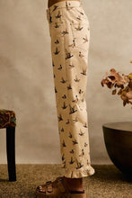 Load image into Gallery viewer, A person wearing cream-colored pants with a black bird print, paired with brown slide sandals, standing in a styled indoor setting.