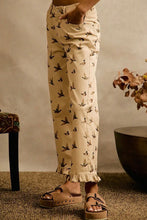 Load image into Gallery viewer, A person wearing beige cropped pants with a black bird print, paired with brown platform sandals, standing in a styled indoor setting with a textured wall and decorative furniture.