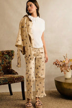 Load image into Gallery viewer, A woman models a beige two-piece pajama set featuring a bird print, consisting of a long-sleeve top and matching pants, styled with a white top and sandals in a cozy room setting.