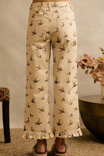 Load image into Gallery viewer, A person wearing cropped wide-leg pants in a warm beige tone with an allover print of small birds, shown from the waist down in a styled indoor setting.