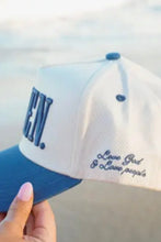 Load image into Gallery viewer, A white and blue baseball cap held by a hand, with 'LOVE GOD &amp; LOVE PEOPLE' embroidered on the side and partial blue lettering on the front, set against a blurred beach background.