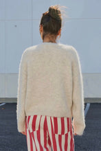 Load image into Gallery viewer, A person viewed from behind wearing a fuzzy off-white knit sweater and red-and-white vertically striped pants, standing outdoors against a pale wall.