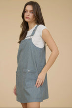 Load image into Gallery viewer, Woman wearing a blue checkered pinafore dress over a white shirt on a beige background
