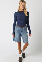 Load image into Gallery viewer, A woman modeling a navy blue long-sleeve top and light-wash denim shorts against a plain light gray studio background.