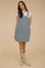 Load image into Gallery viewer, Woman wearing a denim pinafore dress with a plain background