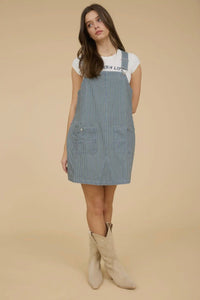 Woman wearing a denim pinafore dress with a plain background