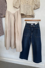Load image into Gallery viewer, Stack of folded jeans and shirts on a white surface