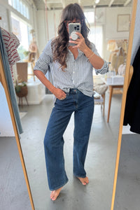 Person taking a mirror selfie wearing a striped shirt and blue jeans in a room.