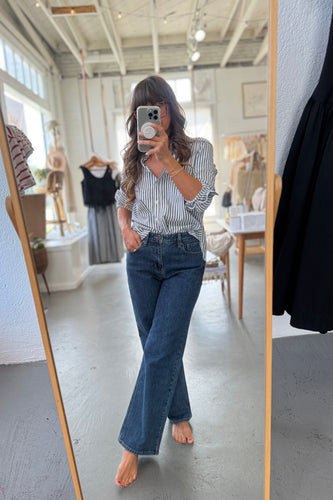 Person taking a mirror selfie wearing a striped shirt and blue jeans in a room with furniture and decor.