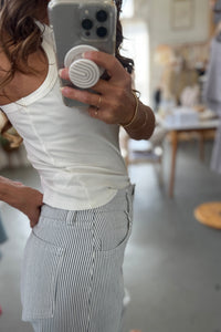 Person taking a mirror selfie wearing a white tank top and striped shorts in a casual setting.
