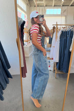 Load image into Gallery viewer, A woman takes a mirror selfie in a clothing boutique, wearing a red and white striped t-shirt, light blue denim overalls, and a white baseball cap with a red heart.