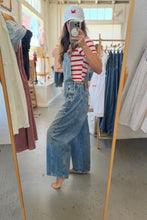 Load image into Gallery viewer, A woman takes a mirror selfie in a clothing boutique wearing light-wash wide-leg denim overalls over a red and white striped t-shirt, paired with a white baseball cap.