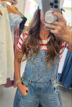 Load image into Gallery viewer, A woman taking a mirror selfie in a clothing store, wearing a light blue denim overall with a red and white striped t-shirt underneath.