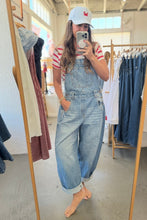 Load image into Gallery viewer, A woman takes a mirror selfie in a clothing boutique wearing light-wash blue denim overalls, a red and white striped t-shirt, a white baseball cap, and is barefoot.