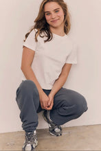 Load image into Gallery viewer, Person wearing a white t-shirt and gray sweatpants sitting against a plain wall.