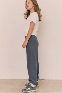 Person wearing a white top and gray pants standing against a plain background