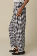 Load image into Gallery viewer, Person wearing black and white checkered pants on a beige background