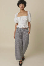 Load image into Gallery viewer, Woman wearing a white top and checkered pants against a beige background