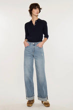 Load image into Gallery viewer, A model stands against a plain white studio background wearing a dark navy long-sleeve polo shirt, light-wash wide-leg blue jeans, and brown suede shoes.