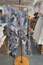 Load image into Gallery viewer, Floral-patterned pants on a hanger in a store setting