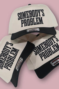Three 'Somebody's Problem' caps on a pink background