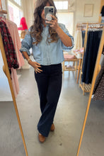 Load image into Gallery viewer, Person taking a mirror selfie wearing a light blue shirt and dark pants in a clothing store.