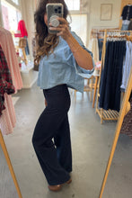 Load image into Gallery viewer, Person taking a mirror selfie wearing a light blue shirt and dark blue jeans in a clothing store.
