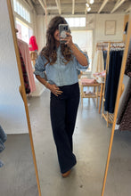 Load image into Gallery viewer, Person taking a mirror selfie wearing a light blue shirt and dark pants in a clothing store.