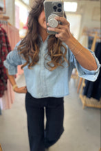 Load image into Gallery viewer, Person wearing a light blue denim shirt and dark pants in a clothing store.