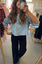 Load image into Gallery viewer, Person wearing a light blue denim shirt and dark pants in a clothing store.