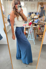 Load image into Gallery viewer, A woman takes a mirror selfie in a clothing boutique, wearing a white sleeveless top and high-waisted, wide-leg blue pants with side pockets.