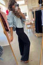 Load image into Gallery viewer, Person taking a mirror selfie wearing a light blue shirt and black pants in a clothing store.