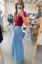 Load image into Gallery viewer, A woman takes a mirror selfie in a clothing boutique, wearing a fitted burgundy short-sleeve top and high-waisted, wide-leg light blue denim jeans.
