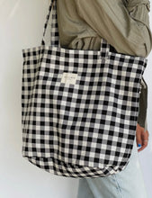 Load image into Gallery viewer, Black and white checkered tote bag held by a person against a plain background