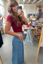 Load image into Gallery viewer, A woman takes a mirror selfie in a clothing boutique, wearing a short-sleeve burgundy top and high-waisted blue wide-leg jeans.