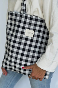 Person holding a black and white checkered bag with 'De La Mar' branding.