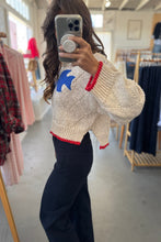 Load image into Gallery viewer, Person wearing a patterned sweater with a blue and red design, taking a mirror selfie in a clothing store.