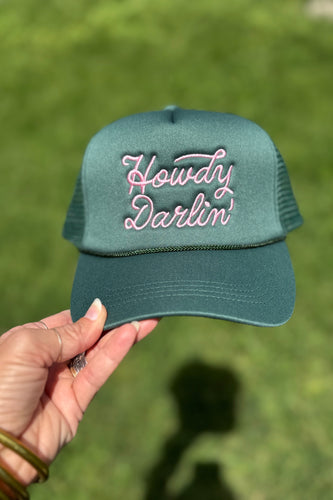 Green cap with 'Howdy Darlin' text held by a hand against a grassy background