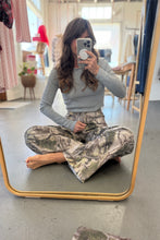 Load image into Gallery viewer, Person wearing camouflage pants and a gray top sitting in front of a mirror.