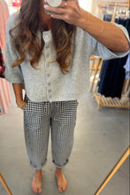 Load image into Gallery viewer, Person wearing a gray button-up shirt and black and white checkered pants in a store setting.