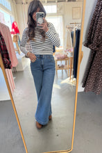 Load image into Gallery viewer, Person taking a mirror selfie wearing a striped shirt and blue jeans in a clothing store.