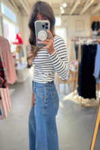 Load image into Gallery viewer, Person taking a mirror selfie wearing a striped shirt and jeans in a clothing store.