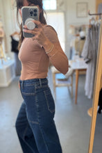 Load image into Gallery viewer, Person wearing a brown top and blue jeans taking a mirror selfie in a store.
