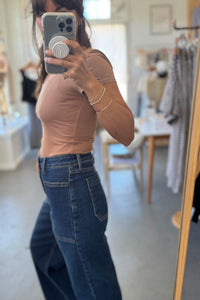 Person wearing a brown top and blue jeans taking a mirror selfie in a store.