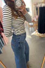 Load image into Gallery viewer, Person wearing a striped shirt and jeans taking a mirror selfie in a clothing store.